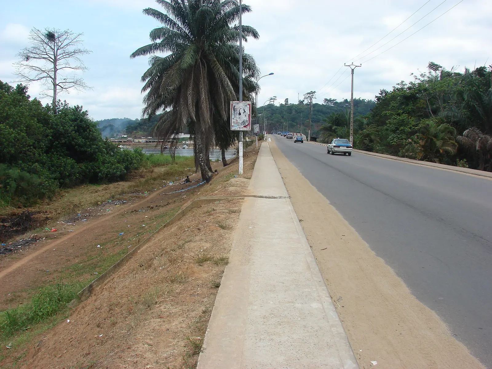 Route bitumée bordée d'un trottoir et de végétation dans le quartier Isaac de Lambaréné