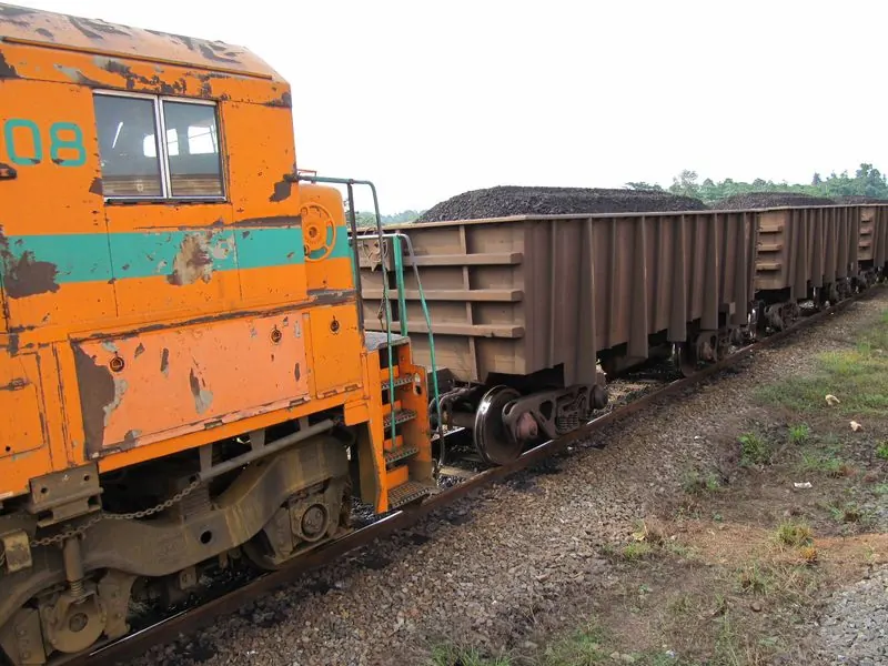 Locomotive orange tirant une rame de wagons chargés de minerai sombre