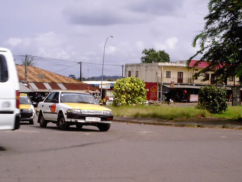Rue commerçante d'Oyem avec un taxi jaune et blanc au premier plan