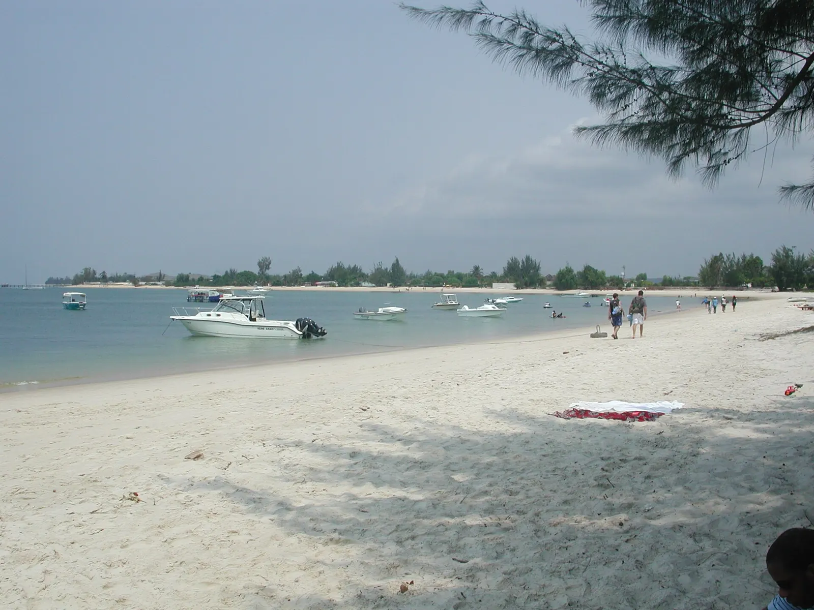 Plage de sable blanc à Pointe Denis avec des bateaux au mouillage et quelques promeneurs